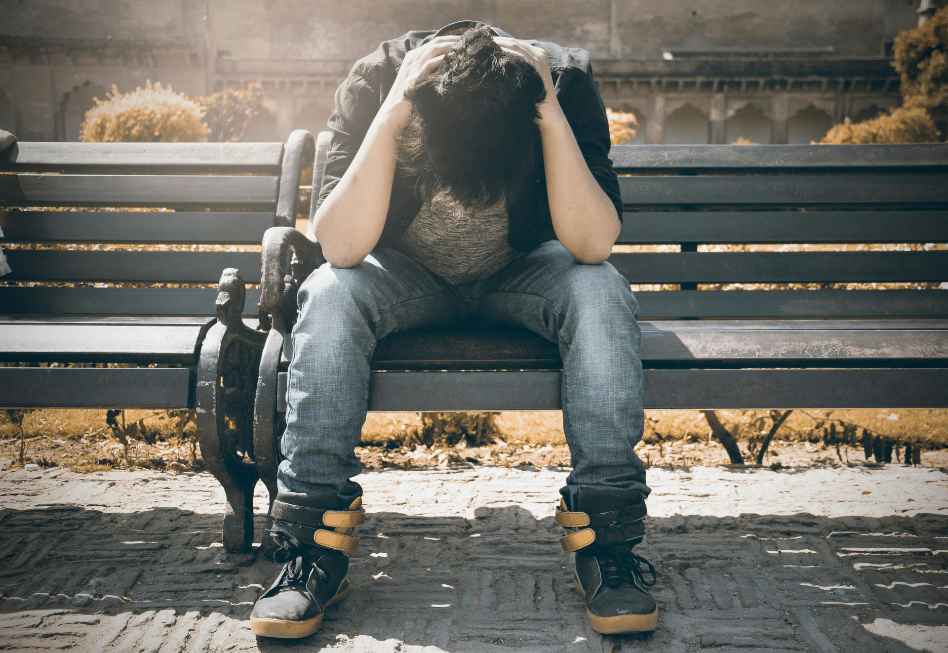 A man sits on an outdoor bench with his head buried in his hands